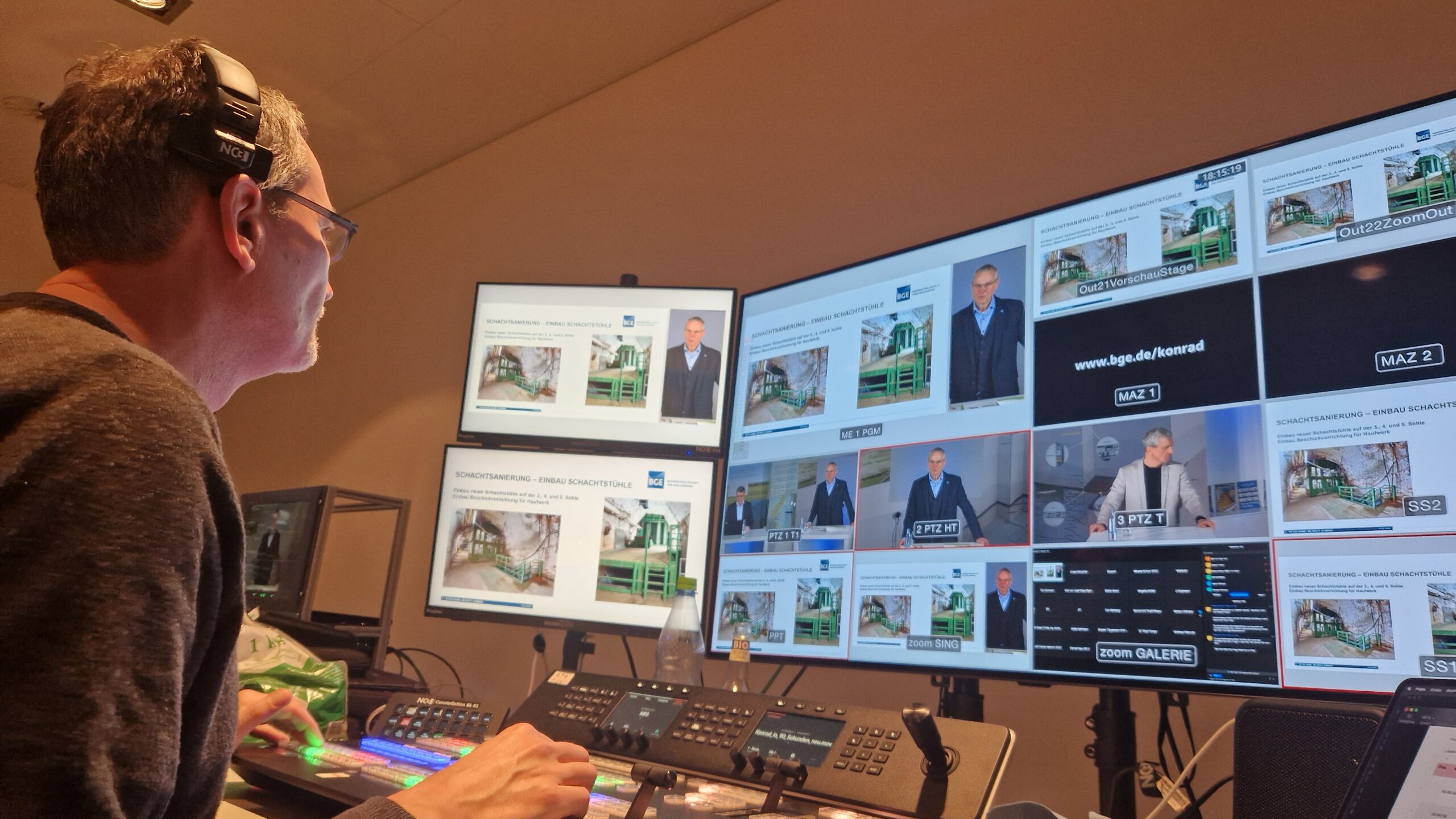 Techniker mit NC3-Kopfhörern überwacht Multi-Monitor-Wall mit Zoom-Galerie und Präsentationen in einem professionellen Streaming-Regieraum.