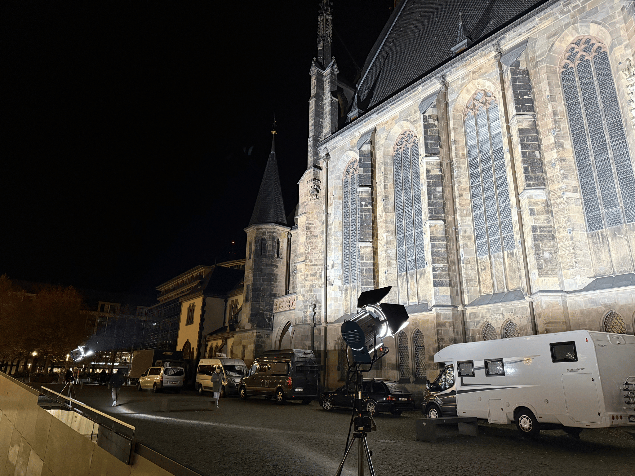 Livestream-Produktion mit Scheinwerfer und Fahrzeugen vor gotischer Kirche bei Nacht