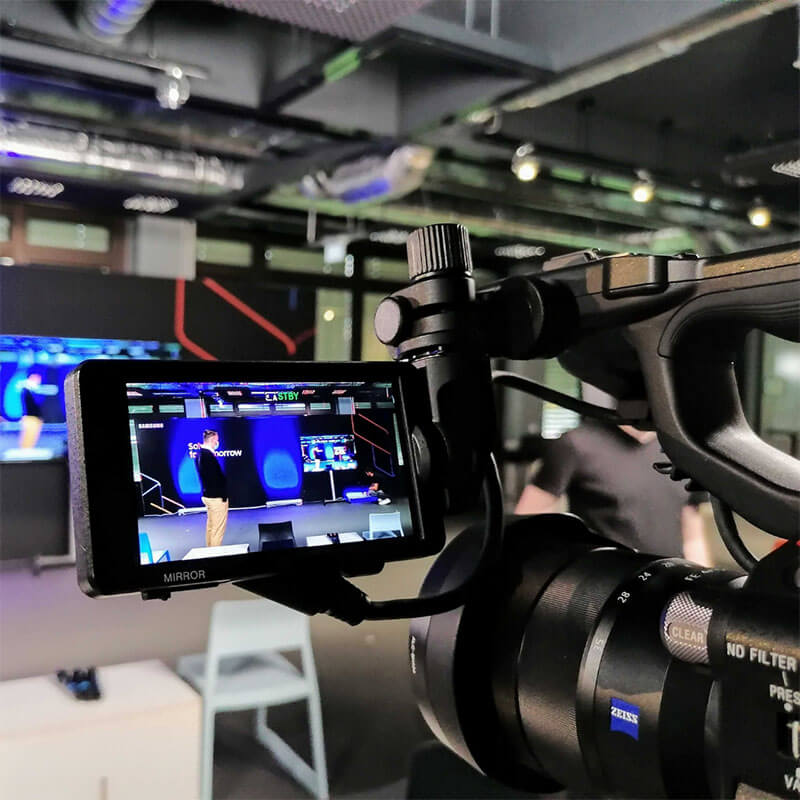 7 Professionelle Kamera mit Flip-Screen zeigt Livestream-Aufnahme eines Moderators auf beleuchteter Bühne