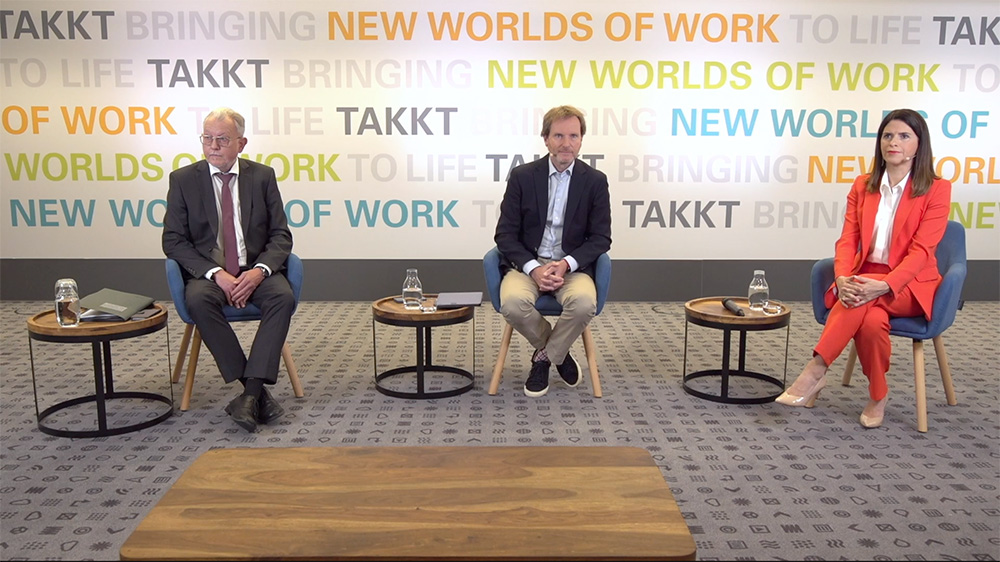 takktag_hv_totale_titelbild Drei Personen auf Bühne bei TAKKTAG mit Hintergrund 'Bringing New Worlds of Work to Life'
