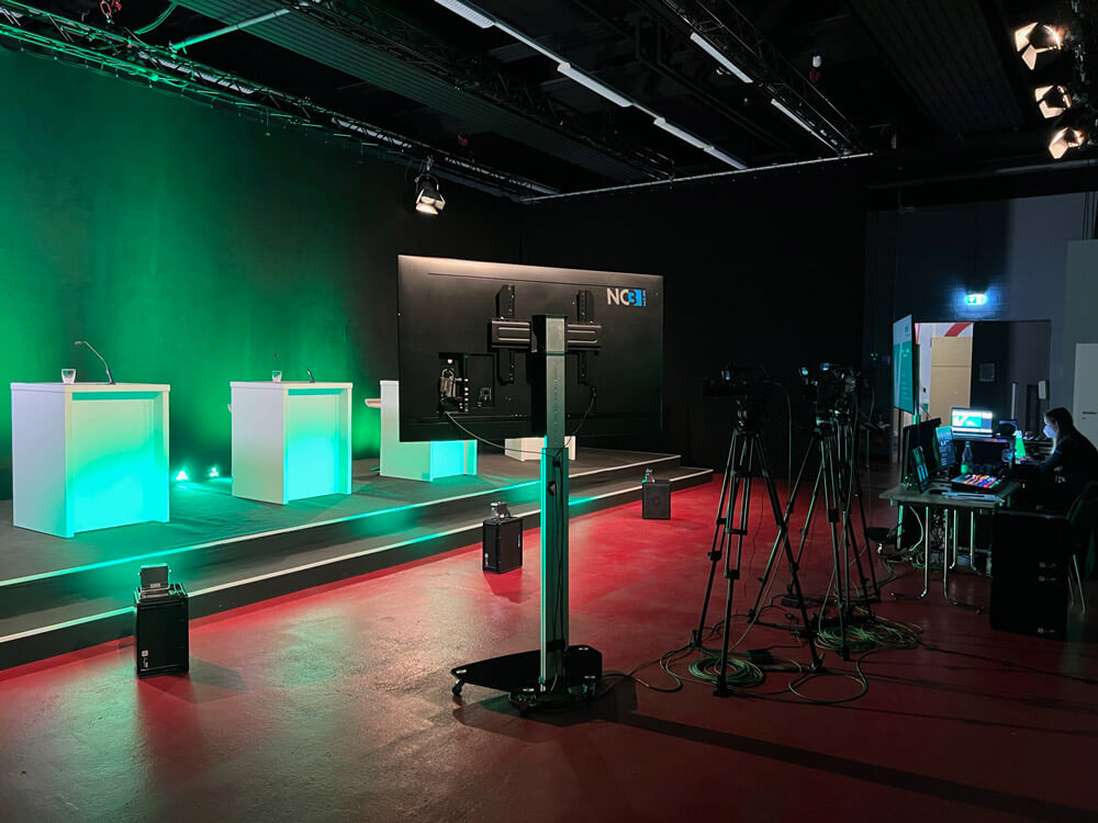 NC3 Studio mit Bühne, beleuchteten Pulten, Green Screen und mehreren Kameras für professionelle Livestreams und Veranstaltungen