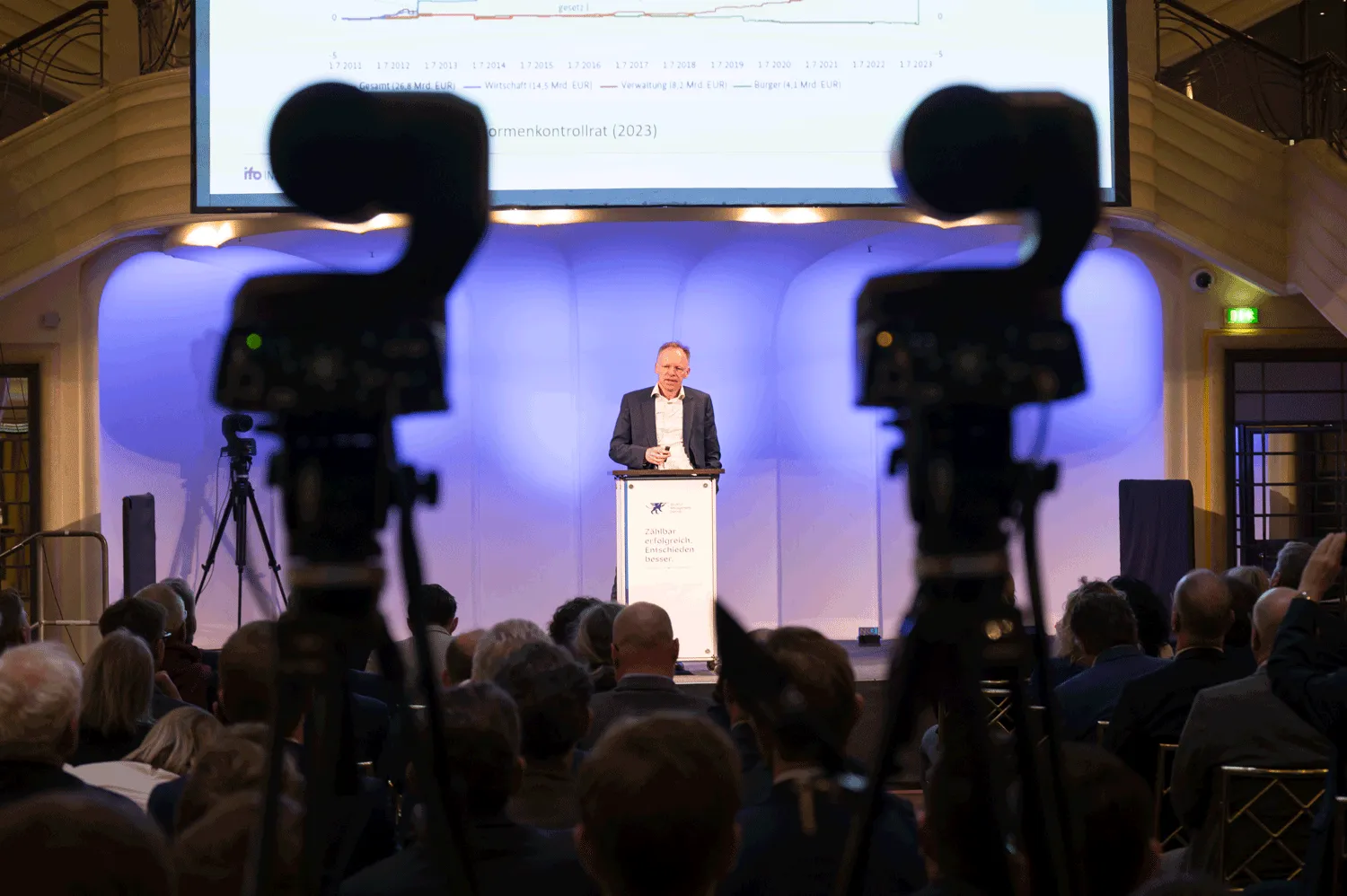 Kamerasicht auf Bühne beim Turnaroundforum mit Redner, Präsentation und Publikum