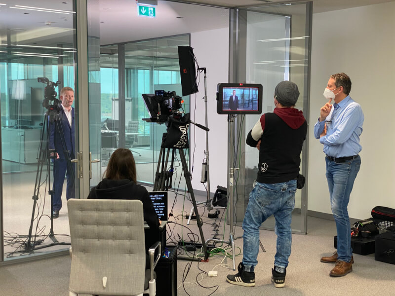 videoproduktion_unternehmenskommunikation Professionelles Videoproduktionsteam bei der Aufnahme eines Unternehmensinterviews in modernem Glasbüro